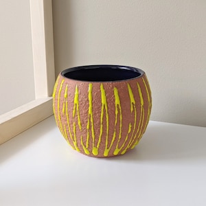 May include: A terracotta planter with a textured surface and yellow paint streaks. The planter has a dark blue glaze on the inside.