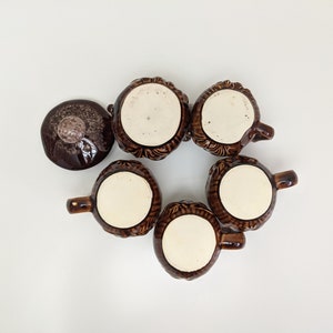 Puede incluir: Seis tazas de cer&aacute;mica marr&oacute;n con un dise&ntilde;o texturizado. Las tazas tienen un interior blanco y est&aacute;n dispuestas en c&iacute;rculo sobre una superficie blanca.