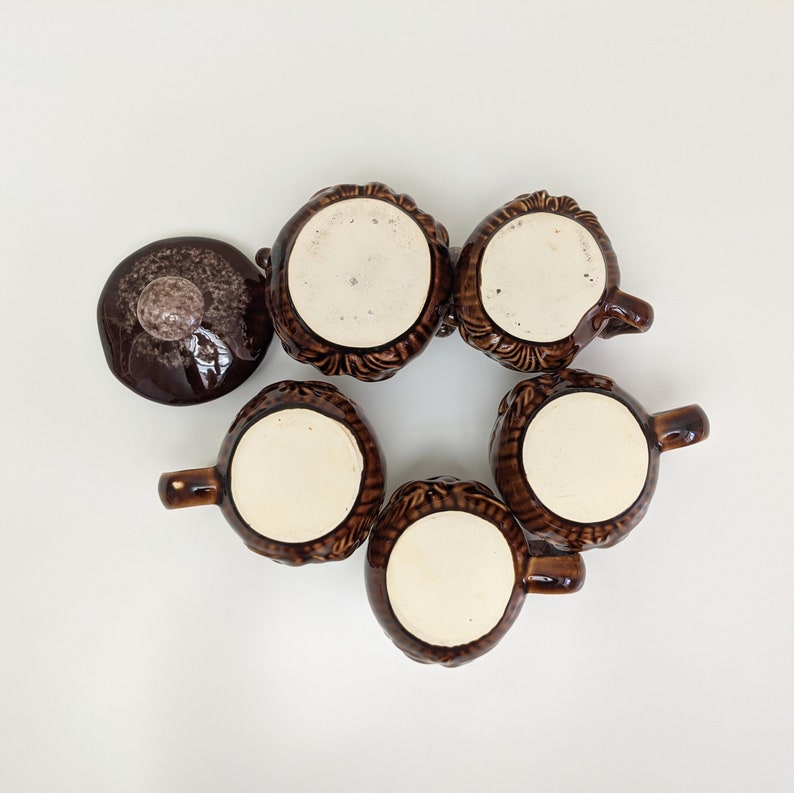 Puede incluir: Seis tazas de cer&aacute;mica marr&oacute;n con un dise&ntilde;o texturizado. Las tazas tienen un interior blanco y est&aacute;n dispuestas en c&iacute;rculo sobre una superficie blanca.