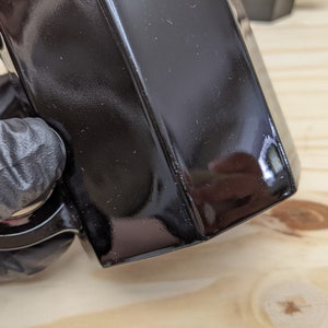 May include: A black ceramic mug with a handle. The mug has a glossy finish and is slightly chipped on the edge.