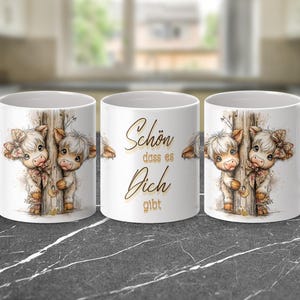 May include: White ceramic mug featuring a watercolor illustration of two Highland cows peeking from behind a wooden post. The mug has a handle and the text "Sch&ouml;n dass es Dich gibt" in gold script.