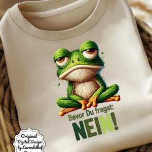 Könnte beinhalten: Beiges Sweatshirt mit einem grimmigen grünen Frosch-Motiv. Der Frosch hat große Augen und sitzt im Schneidersitz. Der Text "Bevor Du fragst: NEIN!" steht in Grün auf dem Shirt. Das Design ist mit "Original Digital Design by Lavendelhof Design" gekennzeichnet.