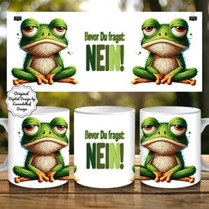 May include: White ceramic mug featuring a grumpy green frog illustration with the text "Bevor Du fragst: NEIN!". The frog has brown eyes and orange feet. The design is repeated on a banner behind the mug.