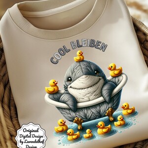 May include: Cream-colored sweatshirt featuring a cartoon shark in a bathtub surrounded by yellow rubber ducks. The shark is gray and white, with the text "COOL BLEIBEN" above it. The design includes the text "Original Digital Design by Lavendelhof Design" and "PNG without Text included".