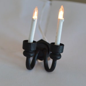 May include: A black metal two-arm sconce with two white light bulbs. The sconce is designed to look like a traditional candlestick.