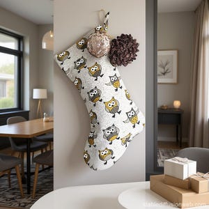 Peut inclure: Une chaussette de Noël avec un motif de hiboux est accrochée au mur, accompagnée d'une boule dorée et d'un élément décoratif marron. La chaussette présente un motif répété de hiboux gris, jaunes et bruns sur fond blanc. La scène se déroule dans une pièce bien éclairée.