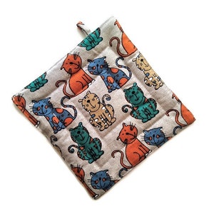 Könnte beinhalten: Ein grauer und weißer Topflappen mit einem Muster aus bunten Comic-Katzen. Die Katzen sind in verschiedenen Posen und haben unterschiedliche Gesichtsausdrücke.