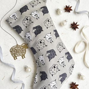 May include: A gray Christmas stocking with a pattern of cartoon sheep in white and dark gray. The stocking is decorated with a gold sheep ornament, silver ribbon, star anise, and small pearl ornaments.
