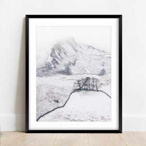 May include: A framed black and white photograph of a snow-covered mountain and valley. A line of trees and a stone wall are in the foreground. The mountain peak is obscured by mist.