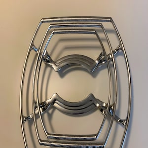 May include: A silver metal cooling rack for hot dishes. The rack is made of three concentric rings, each with a slightly different shape.