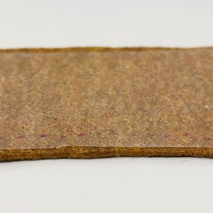 以下が含まれることがあります： 表面がテクスチャ加工され、縁に赤いステッチが施された茶色の革パッチのクローズアップ。