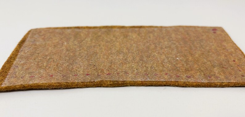 以下が含まれることがあります： 表面がテクスチャ加工され、縁に赤いステッチが施された茶色の革パッチのクローズアップ。