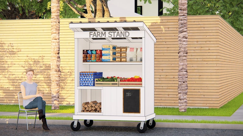 May include: A white farm stand on wheels with the text "FARM STAND" on top. The stand displays various products, including packaged goods, eggs, and fresh produce. A person sits on a chair nearby.
