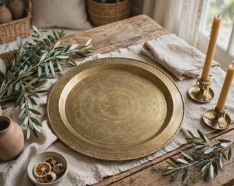 Puede incluir: Una bandeja grande y redonda de latón de estilo antiguo con un motivo circular central y un patrón de borde decorativo punteado. La bandeja tiene un acabado metálico cálido y un borde ligeramente elevado con detalle de cuentas.