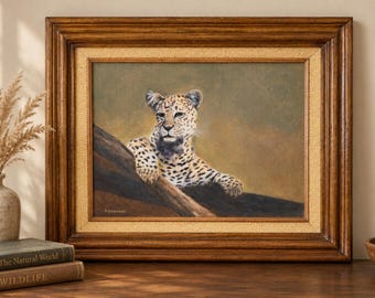 Puede incluir: Un óleo enmarcado que representa a un leopardo descansando sobre una rama de árbol oscura. La obra presenta una paleta de colores beige y marrón con un borde interior texturizado y un marco de madera oscura. Firma visible en la esquina.