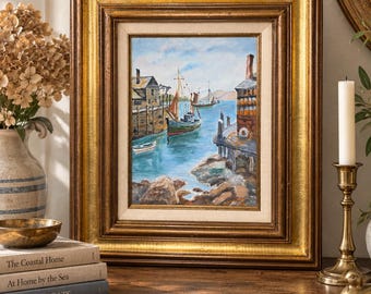 Puede incluir: Una pintura al óleo en un marco grueso y ornamentado de madera dorada y oscura que representa una escena de puerto costero con barcos pesqueros, muelles de madera y edificios bajo un cielo azul. La obra presenta pinceladas texturizadas en tonos azul, marrón y blanco.