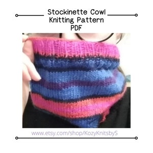 May include: A striped knit cowl in shades of pink, blue, and black. The cowl is folded in half and held by a hand. The text "www.etsy.com/shop/KozyKnitsbyS" is visible at the bottom of the image.