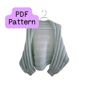 May include: A light green knitted shrug with ribbed sleeves hangs on a white hanger. The garment has a wide, open front and a rounded neckline. A purple cloud-shaped graphic with the words "PDF Pattern" is in the upper left corner.