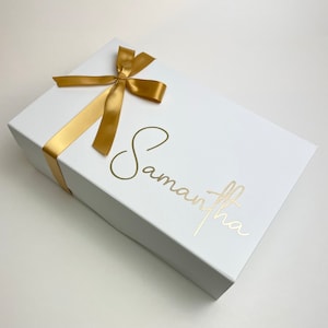 May include: A white gift box with a gold ribbon and bow. The name "Samantha" is written in gold script on the box.