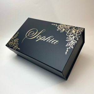 May include: Black gift box with a gold floral design and the name "Sophia" written in cursive.