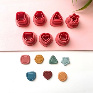 May include: Set of 10 red plastic cookie cutters in various shapes, including a square, circle, hexagon, triangle, star, heart, and oval. The cutters are arranged in two rows on a pink and white surface.
