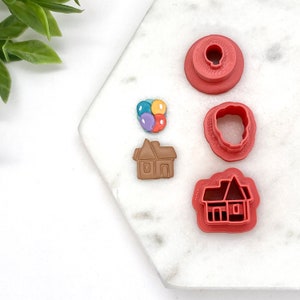 May include: Set of four red plastic cookie cutters shaped like a house, a house with balloons, a cloud, and a circle.