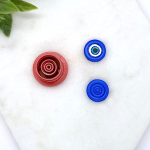 Peut inclure: Trois petits objets décoratifs ronds. L'un est rouge avec des cercles concentriques, l'autre est bleu avec des cercles concentriques et le dernier est bleu avec un œil blanc au centre.