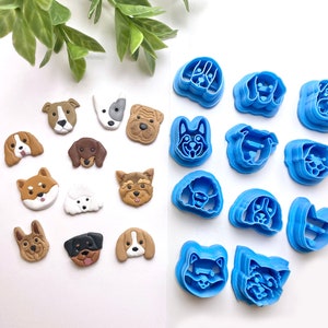 May include: A set of 14 blue plastic dog-shaped cookie cutters and 14 brown and white clay dog figurines. The cutters are arranged in two rows of seven, while the figurines are scattered across the white surface.