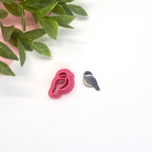 May include: A pink plastic cookie cutter shaped like a bird, and a grey and yellow bird cookie cutter.