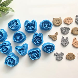 May include: A set of 17 blue plastic dog-shaped cookie cutters and 10 brown and gray dog-shaped cookies. The cutters are arranged in a semi-circle on a white surface. The cookies are arranged in a line below the cutters.