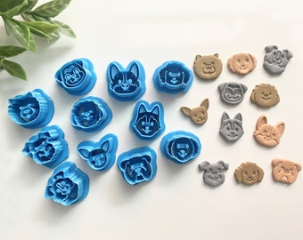 May include: A set of 17 blue plastic dog-shaped cookie cutters and 10 brown and gray dog-shaped cookies. The cutters are arranged in a semi-circle on a white surface. The cookies are arranged in a line below the cutters.
