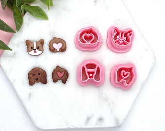 May include: Six pink plastic cookie cutters shaped like dogs and hearts. The cutters are on a white marble surface.
