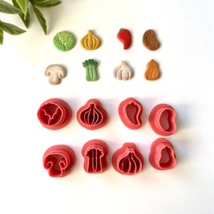 May include: Set of 12 red plastic cookie cutters shaped like vegetables and mushrooms. The cutters include a mushroom, onion, garlic, pepper, celery, and potato.