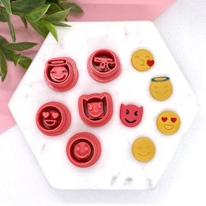 May include: A set of nine red and yellow plastic cookie cutters shaped like various emojis, including a heart-eyed face, a devil face, and a smiling face with a halo.