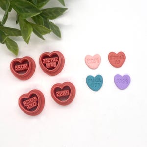 May include: Six red heart-shaped cookie cutters with different phrases: "NOPE", "F**K OFF", "PASS", "SINGLE AF", "NOPE", and "SINGLE AF".  There are also five heart-shaped candies with the phrases: "NOPE", "SINGLE AF", "F**K OFF", "PASS", and "NOPE".