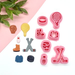 May include: A set of 12 pink plastic cookie cutters shaped like hockey sticks, pucks, skates, a hockey helmet, a jersey, a bowling pin, a boxing glove, and a tennis racket.