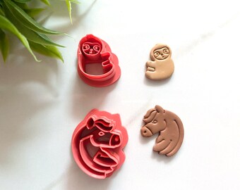May include: Four red and brown plastic cookie cutters shaped like a sloth, a unicorn, and a horse. The cutters are on a white surface.