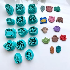 Peut inclure: Une collection d'emporte-pièces en plastique bleu sarcelle représentant divers personnages et objets de dessins animés, accompagnés d'empreintes en pâte à modeler ou en fondant. Le set inclut des formes de visages, d'animaux et d'objets avec le texte Bonnie.