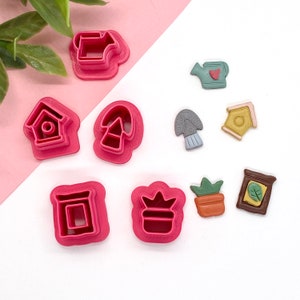 May include: A set of nine pink plastic cookie cutters shaped like a house, a watering can, a mushroom, a flower pot, a plant, a birdhouse, a trowel, and two other shapes.