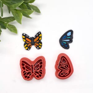 May include: Four butterfly cookie cutters, two red and two black. The red cutters are solid, while the black cutters have a painted design. One black cutter is a monarch butterfly with orange and black wings, and the other is a blue butterfly with blue and green wings.