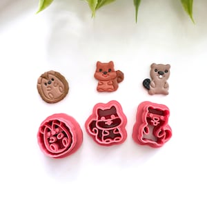 May include: Set of six cookie cutters featuring woodland animal designs. The cutters are pink and feature a squirrel, raccoon, beaver, and hedgehog.
