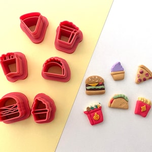 May include: A set of red plastic cookie cutters shaped like various fast food items, including a burger, fries, pizza, taco, ice cream cone, and a cup of popcorn.  Next to the cutters are small, colorful, clay-like replicas of the food items.