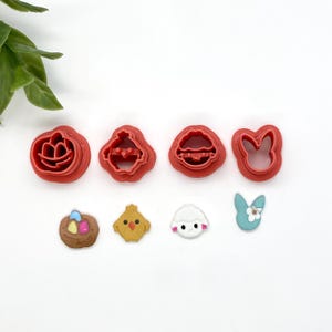May include: A set of six red plastic cookie cutters shaped like a chick, a bunny, a nest with eggs, a lamb, a basket of eggs, and a flower. There are also three fondant decorations: a chick, a lamb, and a bunny.