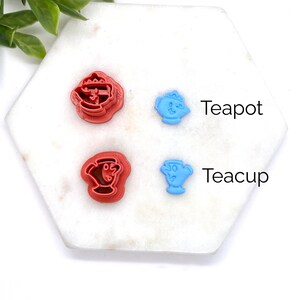 Peut inclure: Deux emportes-pi&egrave;ces en plastique bleu en forme de tasses &agrave; th&eacute; et d'une th&eacute;i&egrave;re, et deux emportes-pi&egrave;ces en plastique rouge en forme de tasses &agrave; th&eacute; et d'une th&eacute;i&egrave;re. Les emportes-pi&egrave;ces sont sur une surface blanche.