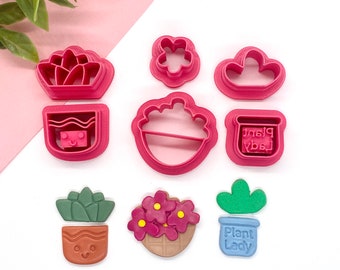 May include: Set of pink plastic cookie cutters in the shape of a flower, cloud, pot, succulent, and a flower pot with flowers. There are also three decorated cookies in the shape of a succulent, a flower pot with flowers, and a cactus.