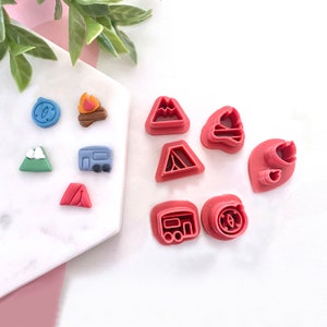 May include: A set of nine red plastic cookie cutters shaped like camping and outdoor adventure icons. The cutters include a compass, a campfire, a mountain, a tent, a camper, a mountain with a snowy peak, and a campfire with a rising plume of smoke.