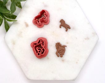 May include: Four horse-shaped cookie cutters on a white hexagonal tile surface. Two of the cutters are red and two are brown.