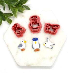 May include: A set of five red plastic cookie cutters shaped like seagulls and a penguin. The penguin cutter has a blue hat.