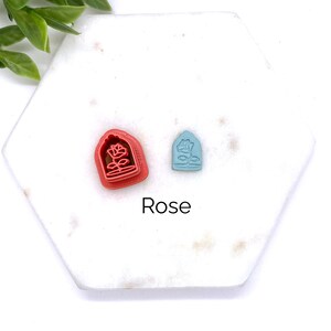 Peut inclure: Deux petits emporte-pi&egrave;ces, l'un rouge et l'autre bleu, en forme de rose dans un d&ocirc;me de verre. Le texte "Rose" est imprim&eacute; sous les emporte-pi&egrave;ces.