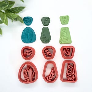 May include: Set of six polymer clay cutters featuring various plant designs. The cutters are in three colors: green, teal, and red. The designs include a cactus, a leaf, and a fern.